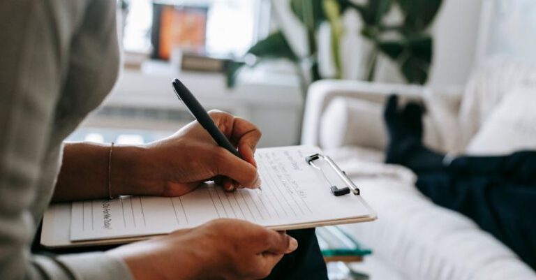 Therapist - Unrecognizable ethnic female therapist taking notes on clipboard while filling out form during psychological appointment with anonymous client lying on blurred background