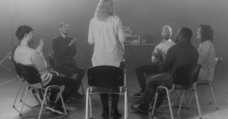 Group Therapy - Woman Standing Beside a Group of People Sitting on Chairs